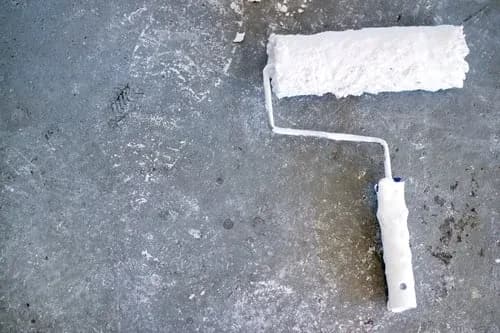 Sealer being rolled onto a cured concrete surface with a long-handled paint roller