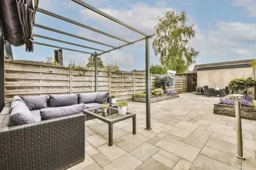 Spacious modern concrete patio with a pergola and lounge seating in a landscaped backyard
