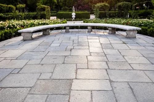 Large finished paver and stone patio with a seating wall bordering a landscaped garden