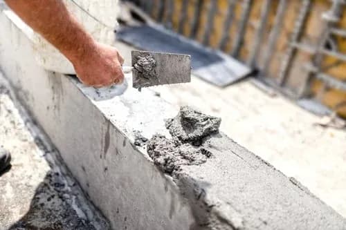 Mason applying repair mortar to a damaged concrete edge with a finishing trowel